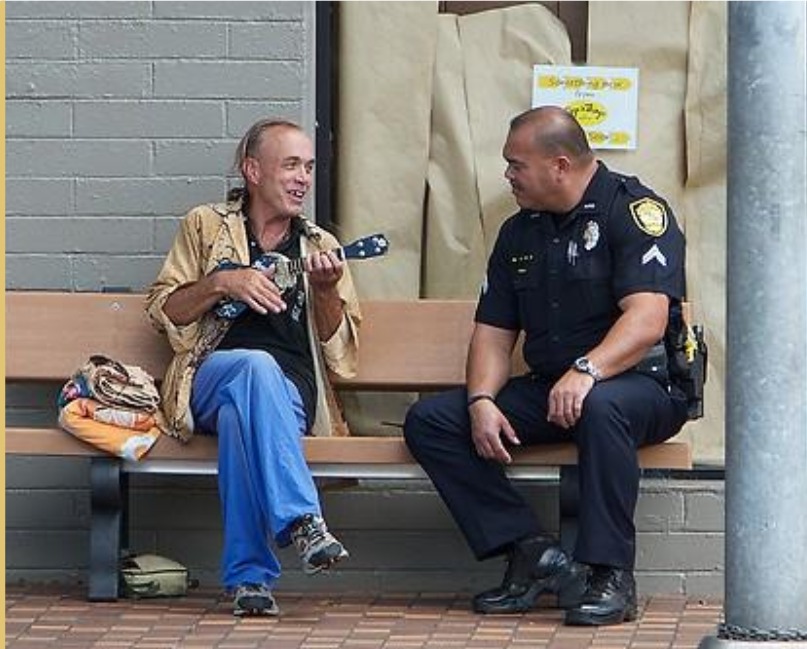 A police officer talking with a man sitting on a bench